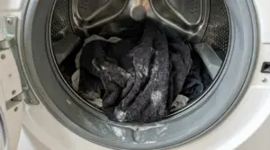 Cestello di lavatrice aperto con panni scuri e residui di detersivo, possibile causa di bucato duro