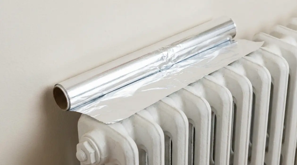 Rotolo di carta stagnola appoggiato su un termosifone bianco vicino alla parete per migliorare la diffusione del calore