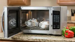 Microonde aperto con carta stagnola, ciotola di vetro, cucchiaio, uovo e contenitore da asporto all’interno