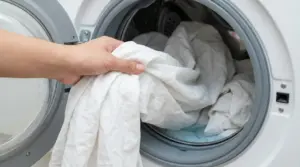 Mano che inserisce lenzuola bianche in una lavatrice a carica frontale per un lavaggio igienizzante