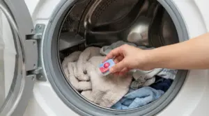 Mano che inserisce una pastiglia per lavastoviglie nel cestello della lavatrice con panni e asciugamani